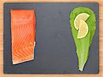 Fresh salmon fish with salad leaf and lemon on stone plate with copy space