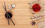 Sushi maki set, herbal tea and sakura branch over bamboo table with copy space