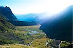 Dawn in Val Veny, with sunlight breaking through mountains and falling on Combal Lake. The region is a stage of the popular Mont Blanc tour.