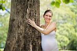 Ecology and environment-Portrait of white pregnant woman in t-shirt embracing and hugging tree in park, smiling and looking at camera