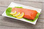 Fresh salmon fish with lemon and salad leaves on wooden table