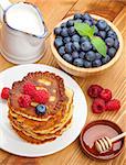 Pancakes with raspberry, blueberry, milk and honey syrup. On wooden table