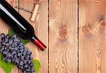 Red wine bottle and bunch of red grapes on wooden table background with copy space