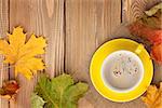 Autumn leaves and coffee cup over wood background with copy space