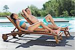 Full length of a young couple sitting on sun loungers by swimming pool