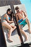 Young couple resting on sun loungers while using digital tablet by swimming pool