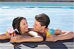 Cheerful young couple with drinks in swimming pool on a sunny day