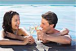 Cheerful young couple toasting champagne in swimming pool on a sunny day
