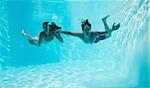 Young couple holding hands and swimming underwater in the swimming pool
