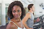 Fit woman smiling at camera on treadmill at the gym