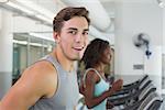 Fit man smiling at camera on treadmill at the gym