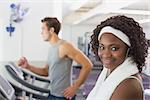 Fit woman smiling at camera on treadmill at the gym