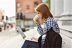 Woman drinking coffee and using laptop outside in the street