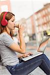 Girl using laptop, listening music and drinking coffee in the street