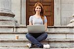 Smiling woman with disposable cup using laptop in the street