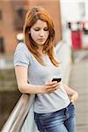 Cheerful redhead with her mobile phone texting a message in the city