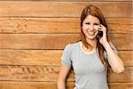 Cheerful redhead leaning against wall phoning in the city