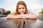 Portrait of a smiling redhead lying on bench in the city