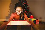 Little girl opening a glowing christmas gift at home in the living room