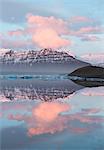 Panoramic view across the calm water of Jokulsarlon glacial lagoon towards snow-capped mountains and icebergs bathed in the last light of a winter's afternoon, at the head of the Breidamerkurjokull Glacier on the edge of the Vatnajokull National Park, South Iceland, Iceland, Polar Regions