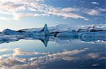 View over Jokulsarlon, a glacial lagoon at the head of the Breidamerkurjokull Glacier, towards icebergs and snow-capped mountains, with reflections in the calm water of the lagoon on a winter's afternoon, on the edge of the Vatnajokull National Park, South Iceland, Iceland, Polar Regions
