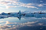 View over Jokulsarlon, a glacial lagoon at the head of the Breidamerkurjokull Glacier, towards icebergs and snow-capped mountains, with reflections in the calm water of the lagoon on a winter's afternoon, on the edge of the Vatnajokull National Park, South Iceland, Iceland, Polar Regions