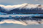 View over Jokulsarlon glacial lagoon towards snow-capped mountains and icebergs, with reflections in the calm water of the lagoon, at the head of the Breidamerkurjokull Glacier on the edge of the Vatnajokull National Park, South Iceland, Iceland, Polar Regions