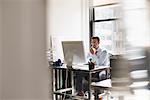 A man seated at a desk in an office, using a computer.