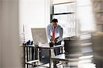 A man standing at his desk using his phone, dialling or texting.