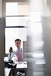 A man working at an office computer, holding a smart phone up to check for messages.