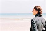 A woman in a grey jacket looking out over a beach and the sea.