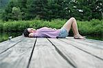 A woman lying on the jetty by a lake in summer