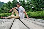 A man sitting on a wooden pier by a lake in summer