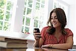 A woman seated at a table, checking her smart phone.