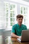 A man seated at a table using a laptop. Working from home.