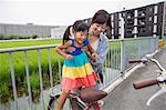 A mother lifting her daughter onto a bicycle.