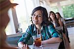 A woman seated at a diner looking at her companion. A long cool drink with a straw.