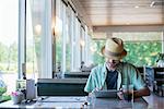 A man wearing a hat sitting in a diner using a digital tablet.