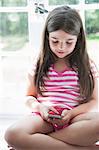 A girl sitting playing, holding a smart phone.