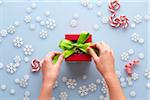 Overhead View of Hands Tying Bow on Present with Snowflakes and Candy Cane Swirls, Studio Shot