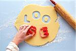 Overhead View of Woman's Hand using Cookie Cutters to spell LOOSE in Rolled out Suger Cookie Dough, Studio Shot