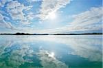 Blue sky, clouds and sun reflected in lake, Lake Woerthsee, Bavaria, Germany