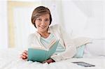 Smiling woman reading book on bed