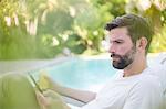 Man using digital tablet and drinking juice by swimming pool