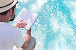 Man reading book over swimming pool