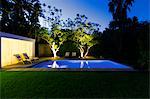 Illuminated swimming pool and trees in backyard at dusk