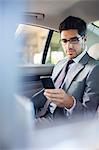 Businessman using cell phone in car back seat