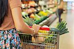 Close up of woman pushing full shopping cart in grocery store