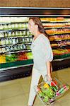 Blurred view of woman carrying full shopping basket in grocery store