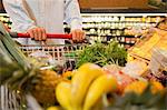 Close up of man pushing full shopping cart in grocery store